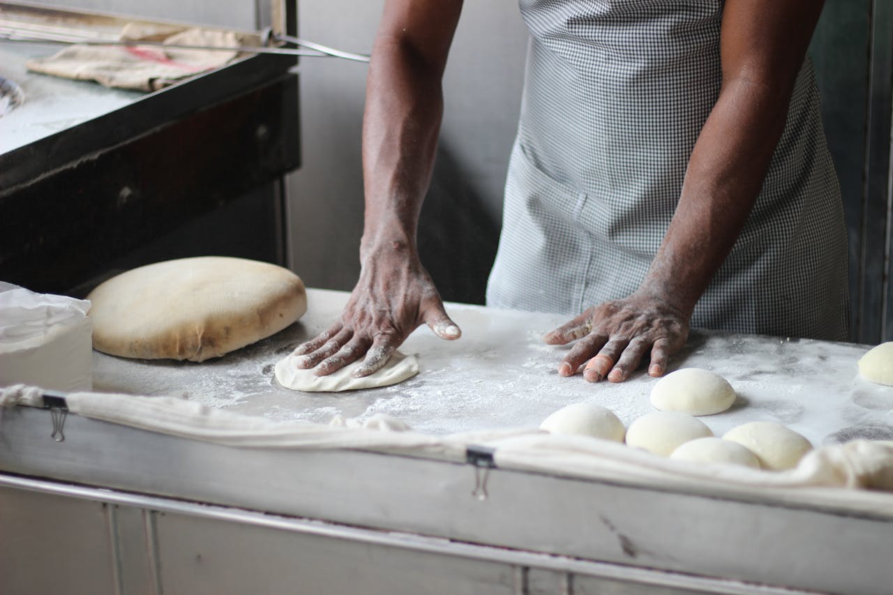 collection-01 A baker in an indoor kitchen kneading dough for bread preparation, showcasing traditional baking techniques.