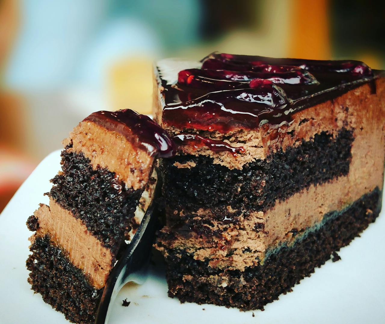 our-mission-01 Close-up of a rich chocolate cake slice with blueberry topping, perfect for dessert lovers.